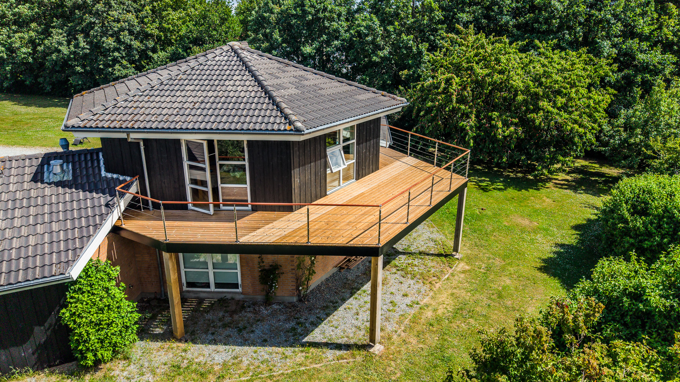 Terrasse surélevée en bois avec une balustrade en câble métallique qui épouse la forme de la maison au niveau des angles, vue d'en haut.