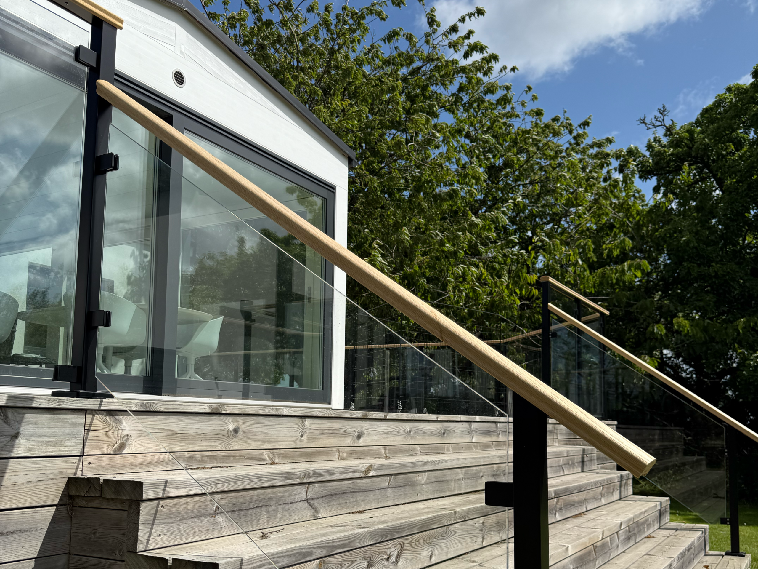 Escalier avec garde-corps en verre et main courante en bois installée le long de la pente de l'escalier.