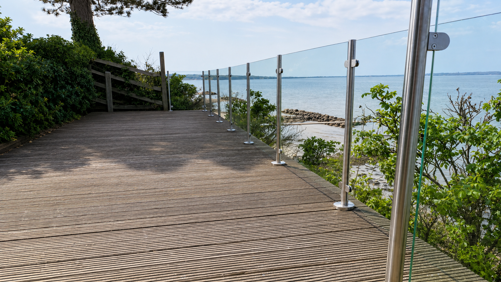 Glasräcke med rostfria stolpar på terrass med fri sikt mot havet.
