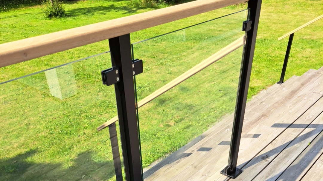 Garde-corps en verre avec montants noirs et traverses en bois, fixé sur une terrasse en bois et ancré à la structure porteuse de la terrasse