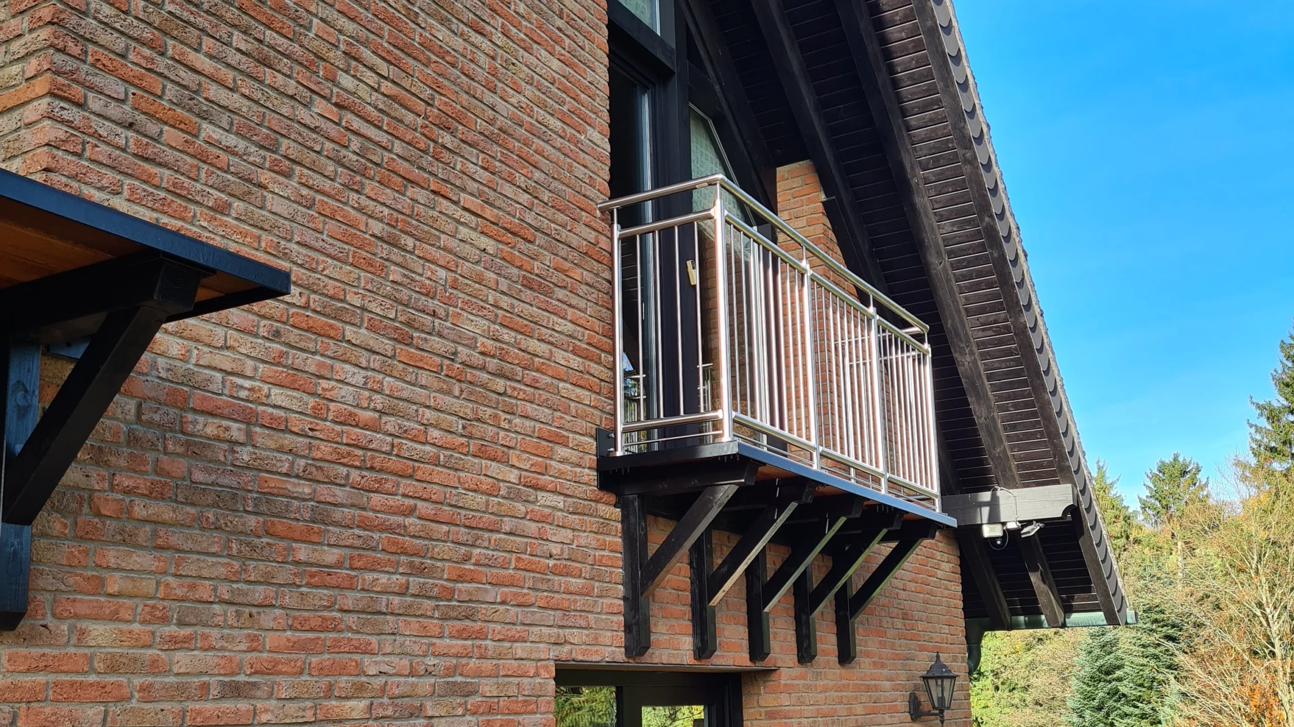 Petit balcon avec une balustrade en acier inoxydable sur une façade en briques ancienne, illustrant comment un balcon sans balustrade peut être équipé d'un dispositif de protection contre les chutes adapté.