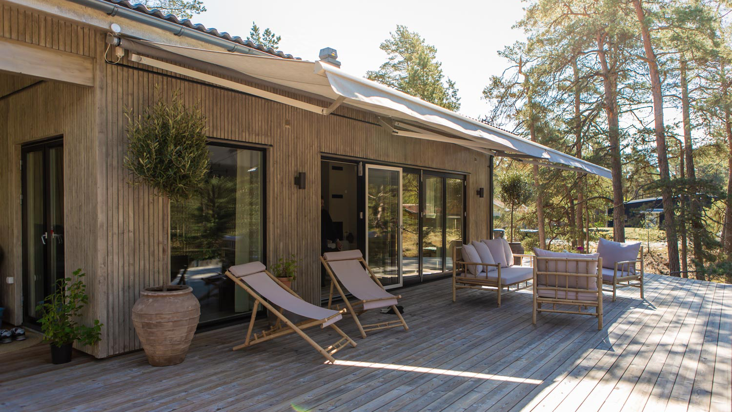 Ljusgrå terrassmarkis utfälld över trädäck med loungemöbler och solsängar.