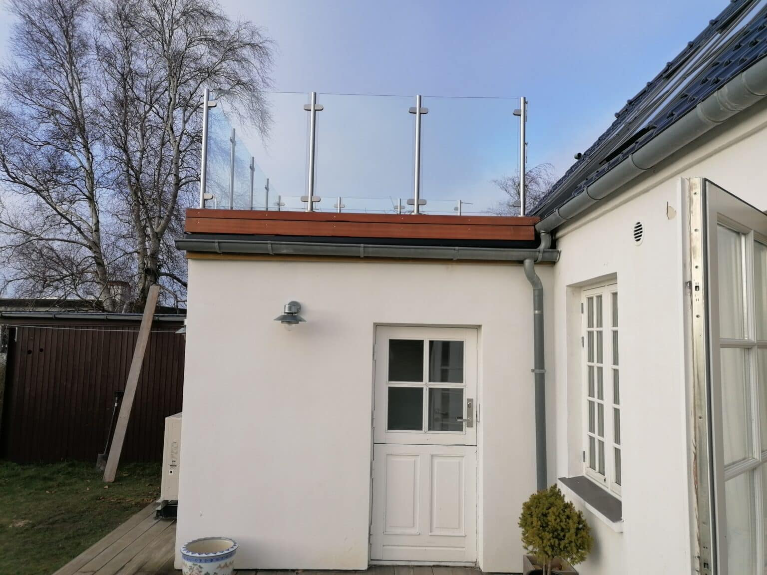 Glasräcke på platt tak till ett vitt hus med måttanpassad infästning längs takets kant.