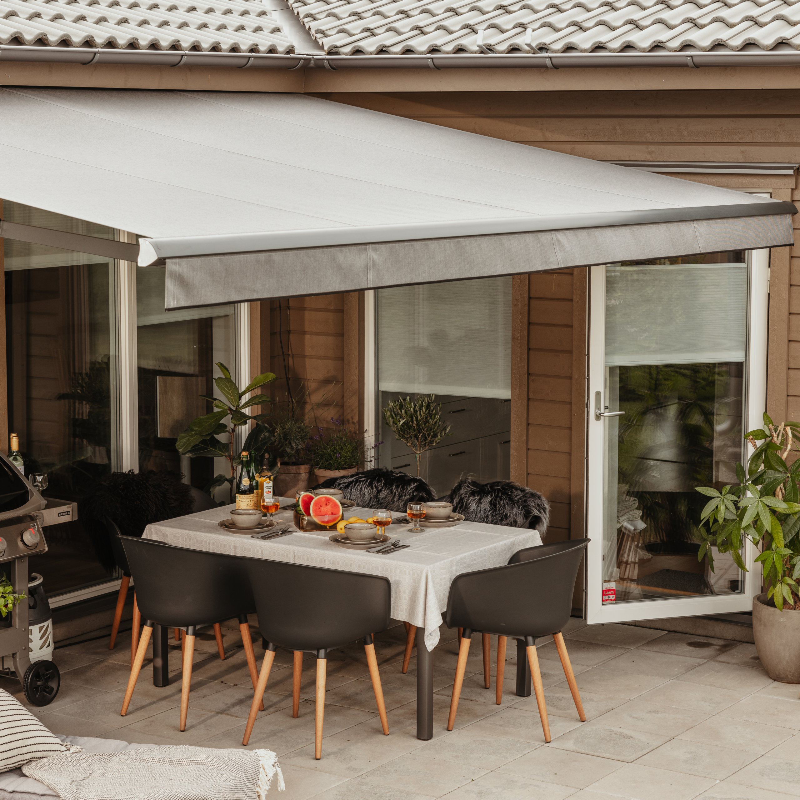 Terrassmarkis som skapar skugga över uteplats med grill och sittplats