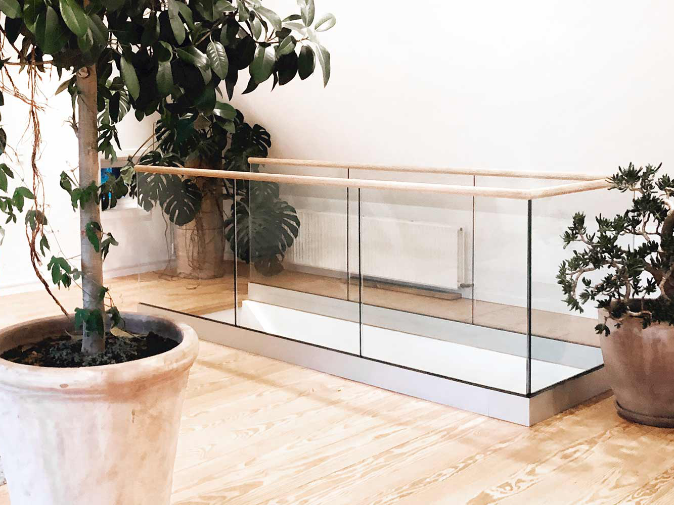 Indoor glass railing by a staircase, featuring plants and light-colored decor.